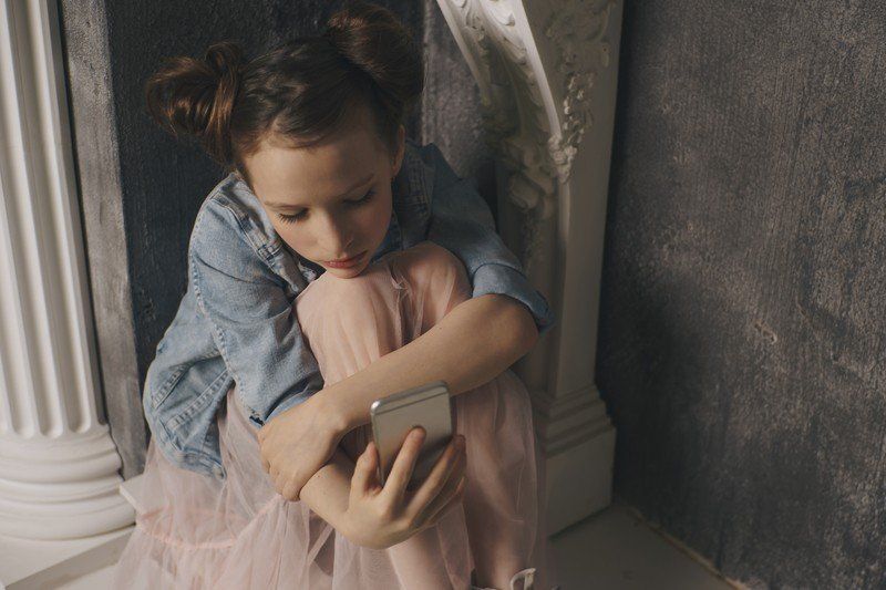 A little girl is sitting on the floor using a cell phone.